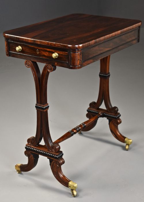 fig 2. An early nineteenth-century rosewood occasional table featuring a rectangular top with a single drawer, scrolled trestle supports, beaded mouldings, and brass castors.