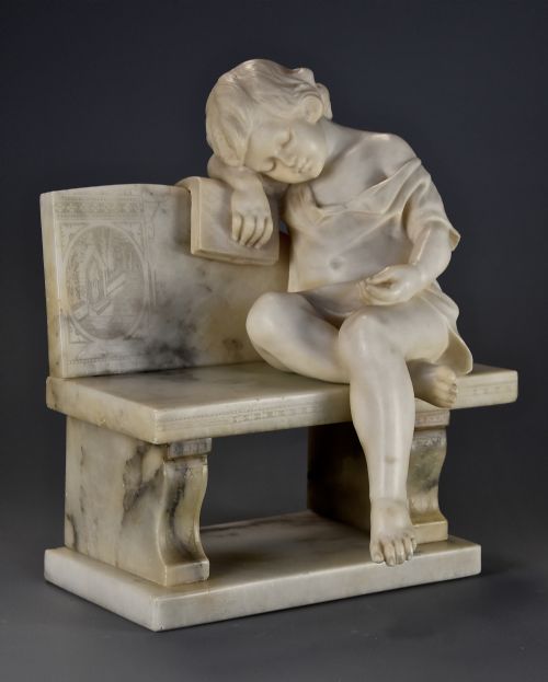 fig 1. A late 19th-century carved alabaster sculpture depicting a sleeping child seated on a bench and resting against a book.