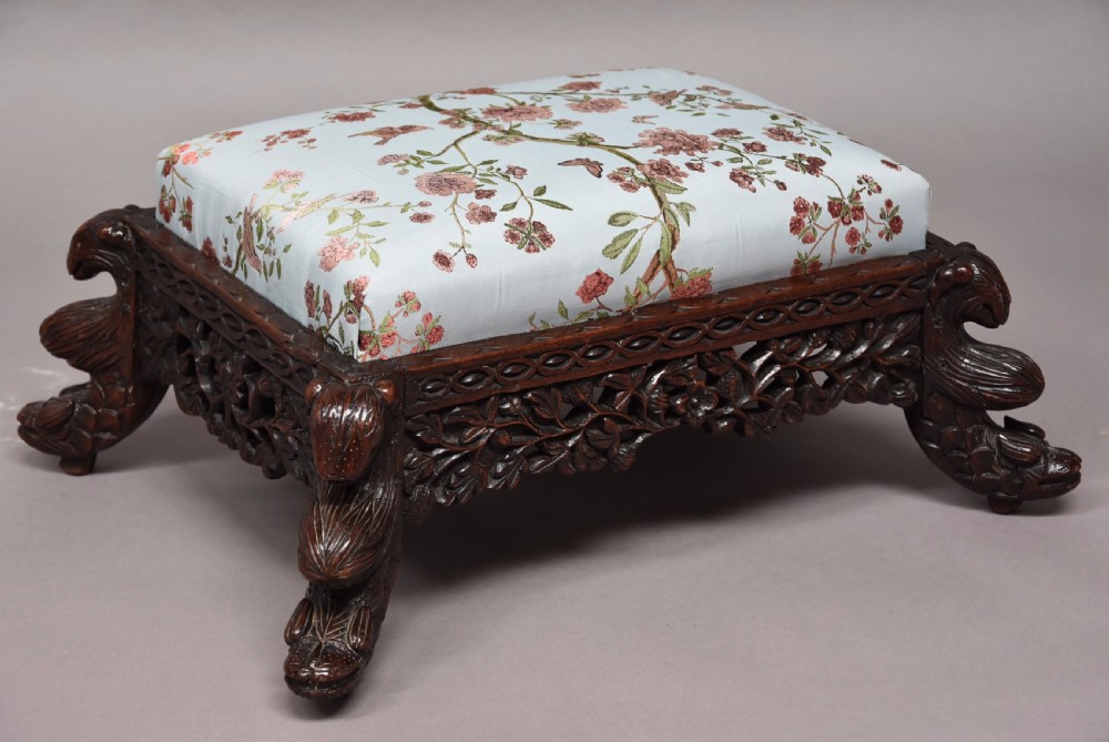 A late 19th-century Anglo-Indian dark hardwood footstool with intricately carved floral aprons, zoomorphic legs, and a light blue floral upholstered seat. View III