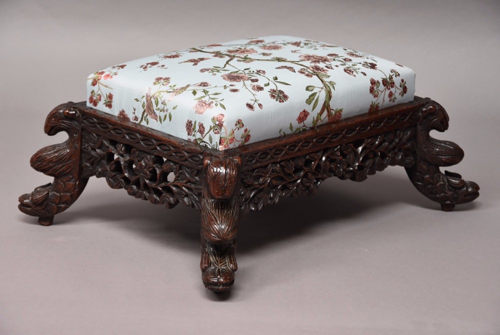 A late 19th-century Anglo-Indian dark hardwood footstool with intricately carved floral aprons, zoomorphic legs, and a light blue floral upholstered seat. View IV