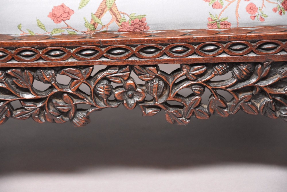 A late 19th-century Anglo-Indian dark hardwood footstool with intricately carved floral aprons, zoomorphic legs, and a light blue floral upholstered seat. View VII