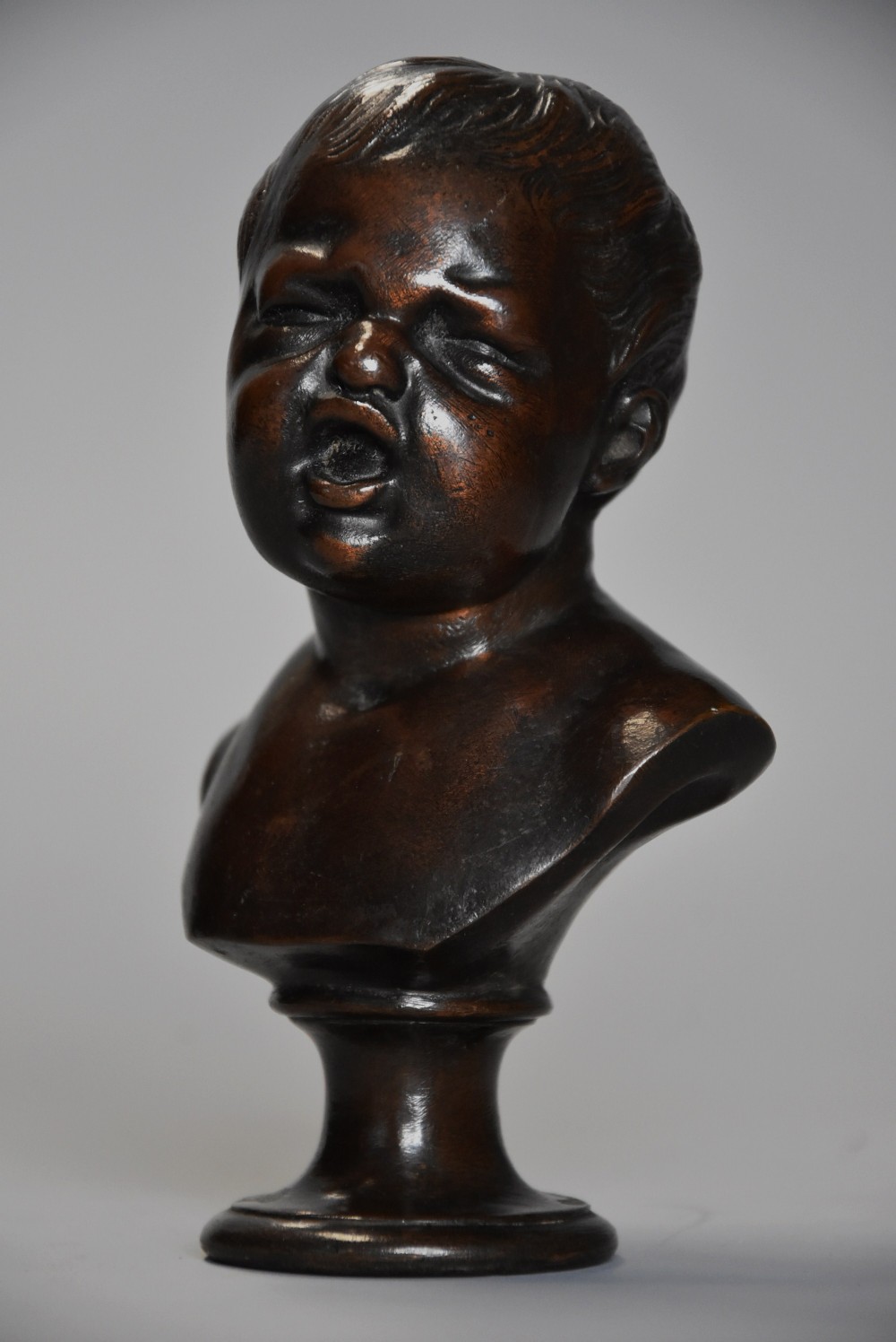 A late nineteenth-century dark brown patinated bronze bust depicting a young child with an open mouth, set on a turned circular socle.
