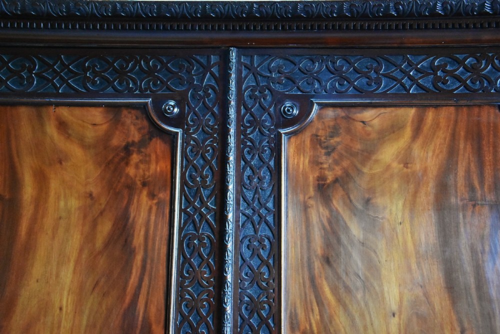 A mid-nineteenth century mahogany press cupboard featuring carved double doors with flame mahogany panels over a base of carved drawers with brass handles. View VI