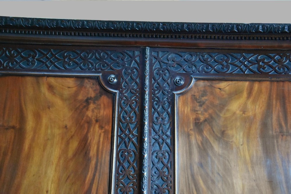 A mid-nineteenth century mahogany press cupboard featuring carved double doors with flame mahogany panels over a base of carved drawers with brass handles. View X