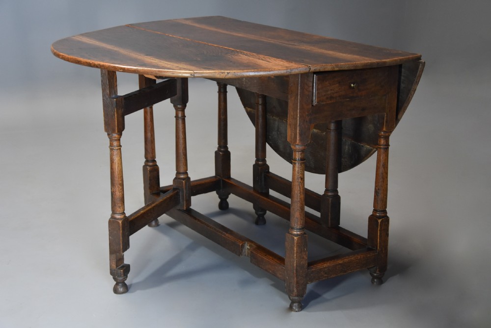 An early 18th century oak gateleg table with a rounded drop-leaf top, turned legs, and lower stretchers. View V