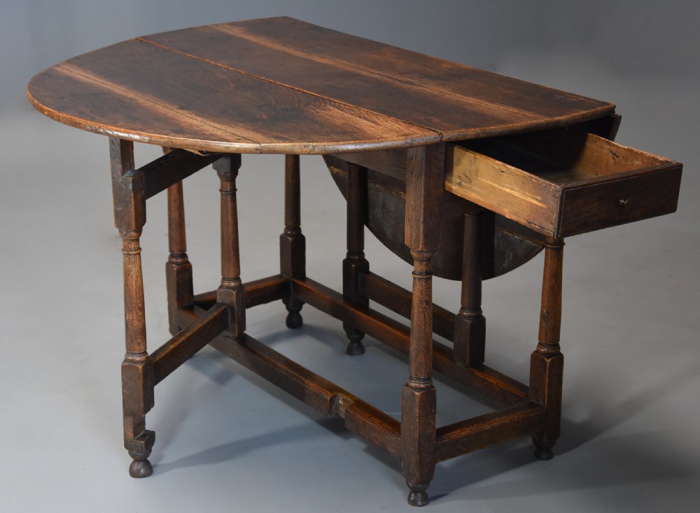An early 18th century oak gateleg table with a rounded drop-leaf top, turned legs, and lower stretchers. View VI