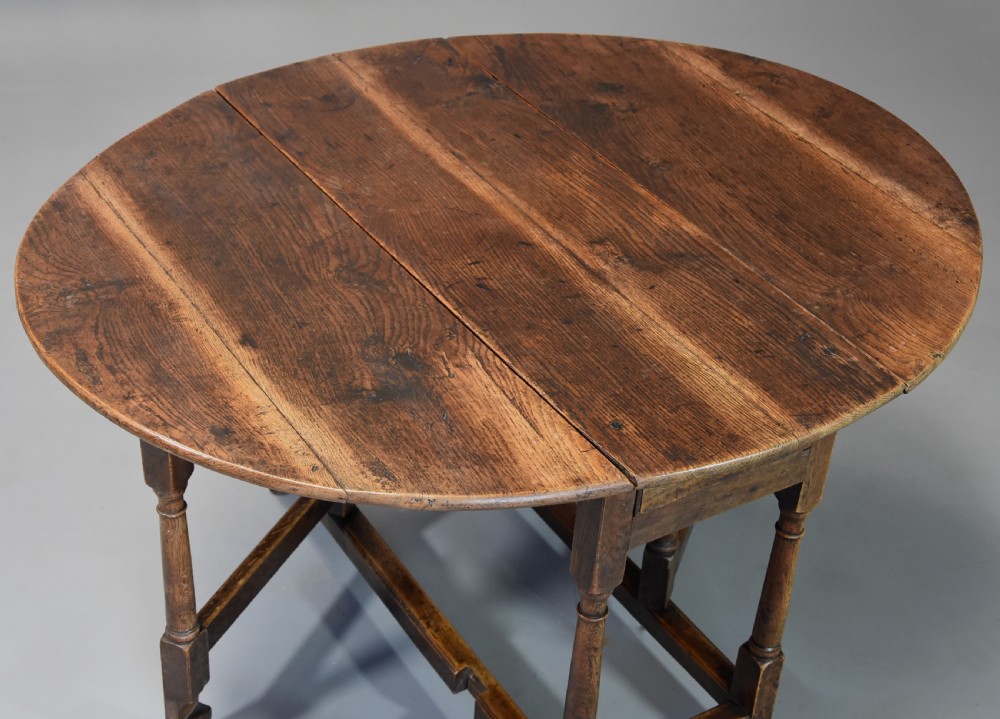 An early 18th century oak gateleg table with a rounded drop-leaf top, turned legs, and lower stretchers. View VII