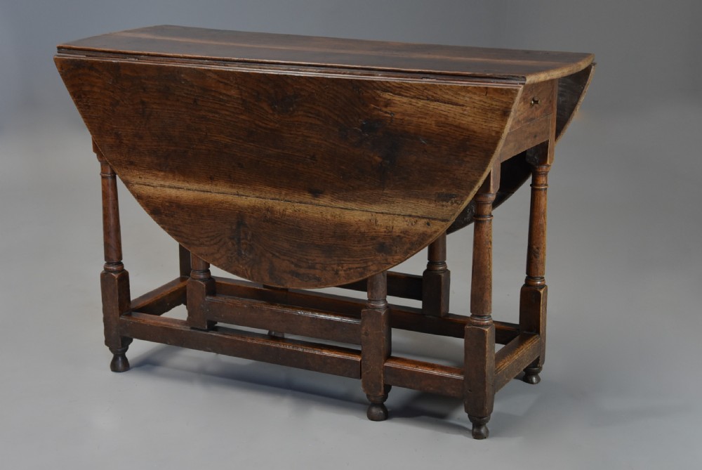 An early 18th century oak gateleg table with a rounded drop-leaf top, turned legs, and lower stretchers. View IX