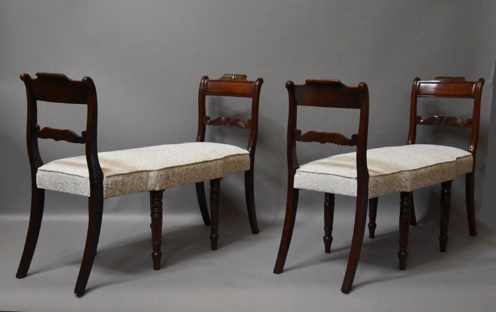 A pair of early nineteenth-century mahogany window seats with carved backrails at each end, turned legs, and cream fabric seats.