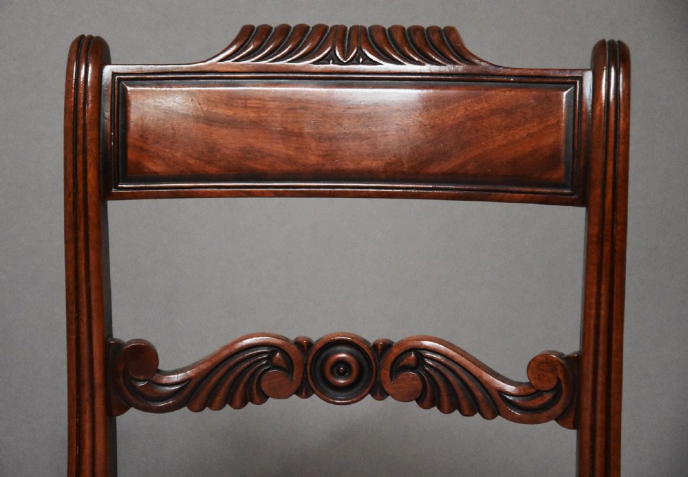 A pair of early nineteenth-century mahogany window seats with carved backrails at each end, turned legs, and cream fabric seats. View V