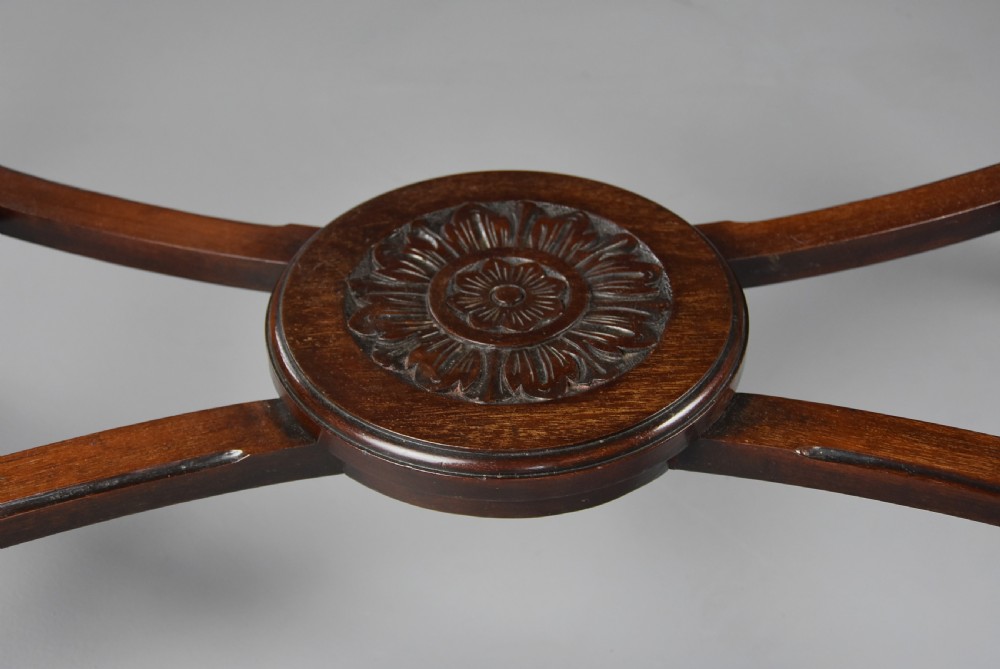 An antique dark mahogany centre table featuring intricate relief carvings on the top, a shaped carved apron, and an X-frame stretcher with a central roundel. View X