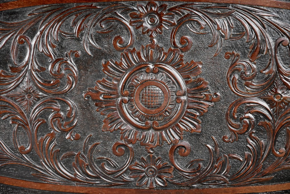 An antique dark mahogany centre table featuring intricate relief carvings on the top, a shaped carved apron, and an X-frame stretcher with a central roundel. View XII