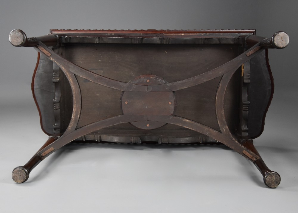 An antique dark mahogany centre table featuring intricate relief carvings on the top, a shaped carved apron, and an X-frame stretcher with a central roundel. View XIV