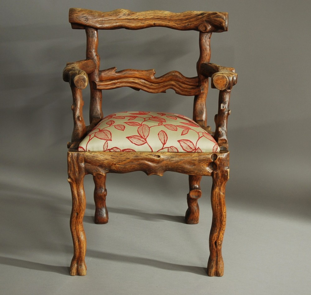 A mid-19th-century carved elm armchair featuring a branch-like naturalistic wooden frame and a cream upholstered seat with red leaf motifs.