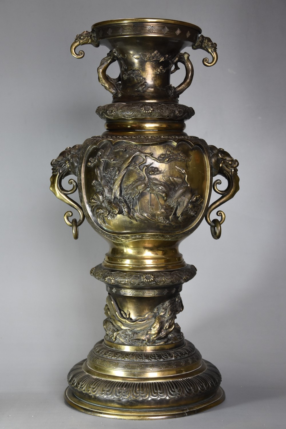 A large 19th-century Japanese Meiji period patinated bronze vase with relief carvings of birds, dragon head handles, and decorative patterned borders.