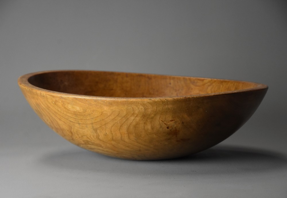 A shallow hand-turned sycamore wooden dairy bowl showing natural grain patterns and a warm honey-brown finish.