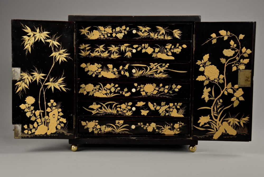 A small rectangular black lacquer table cabinet featuring hand-painted gilt floral and bird decoration with brass bun feet. View X