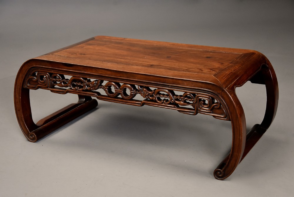 An early 20th-century rectangular Chinese low table crafted from warm brown padouk wood, featuring a carved openwork apron and rounded legs with scroll feet.