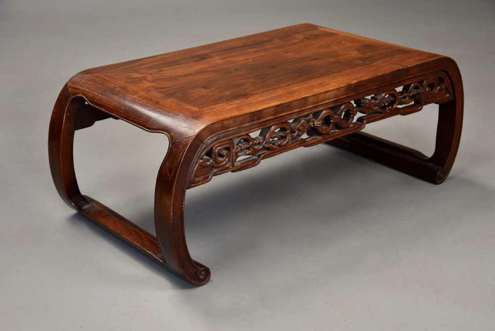 An early 20th-century rectangular Chinese low table crafted from warm brown padouk wood, featuring a carved openwork apron and rounded legs with scroll feet. View VI