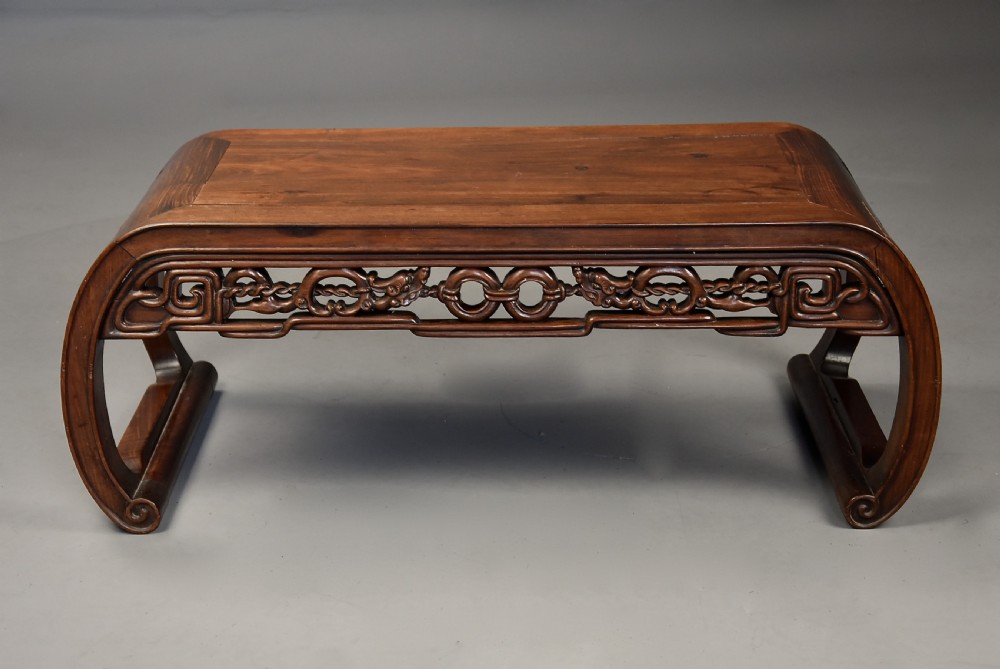 An early 20th-century rectangular Chinese low table crafted from warm brown padouk wood, featuring a carved openwork apron and rounded legs with scroll feet. View X
