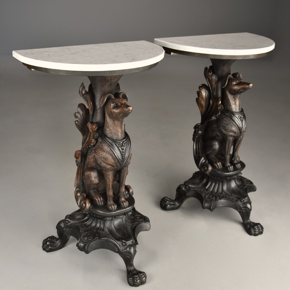 Pair of late 19th-century Black Forest demilune side tables featuring carved seated hound pedestals and white marble tops.
