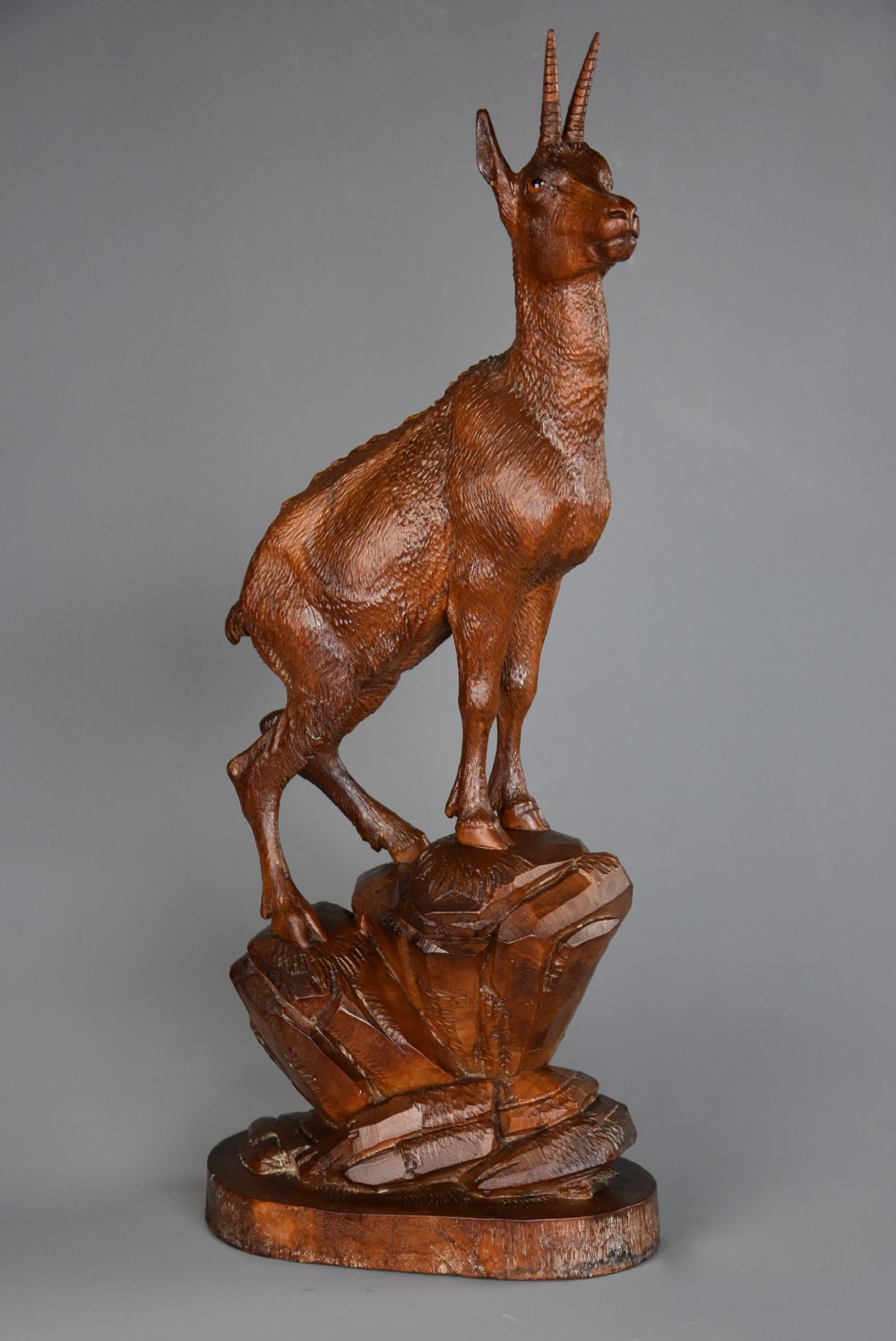 A late nineteenth-century hand-carved linden wood sculpture of a female ibex standing on a rocky naturalistic base.