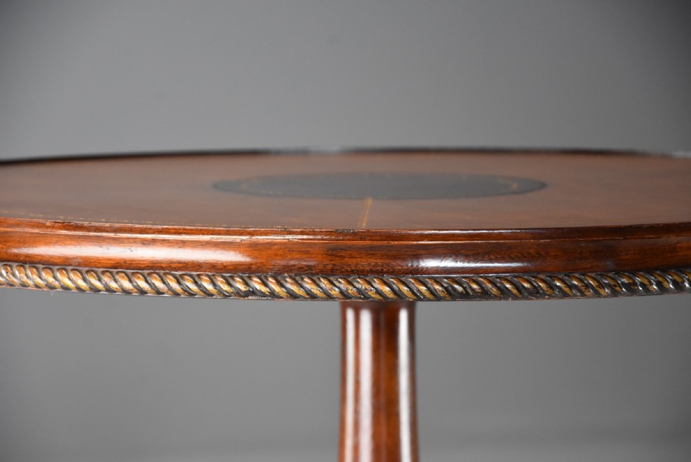 A round mahogany tripod table featuring a brown leather inset top with a rope-twist border, supported by an acanthus leaf carved stem and three scrolled legs. View VIII