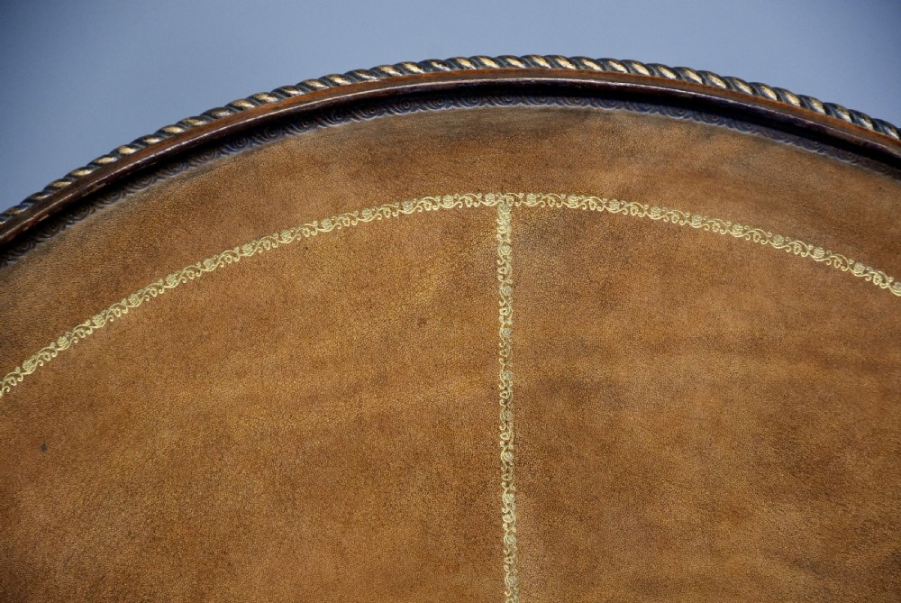 A round mahogany tripod table featuring a brown leather inset top with a rope-twist border, supported by an acanthus leaf carved stem and three scrolled legs. View X