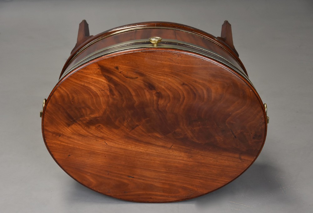 Late eighteenth-century oval mahogany cellarette featuring wide brass binding, side drop handles, and tapered square legs with brass castors. View XI