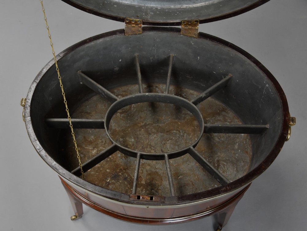 Late eighteenth-century oval mahogany cellarette featuring wide brass binding, side drop handles, and tapered square legs with brass castors. View XIII