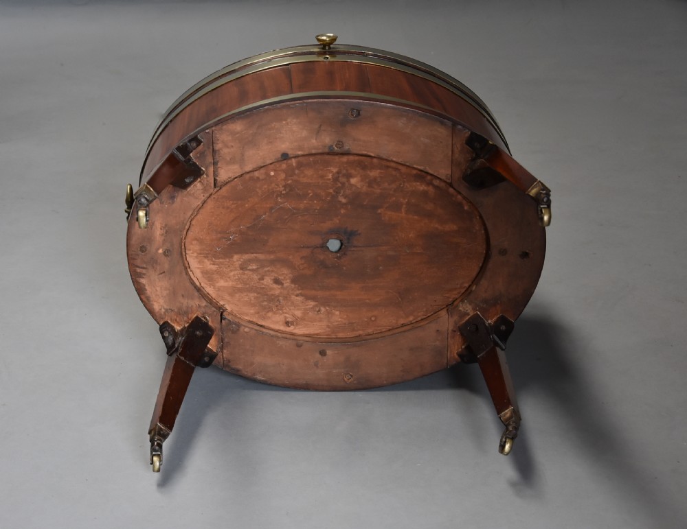 Late eighteenth-century oval mahogany cellarette featuring wide brass binding, side drop handles, and tapered square legs with brass castors. View XVII