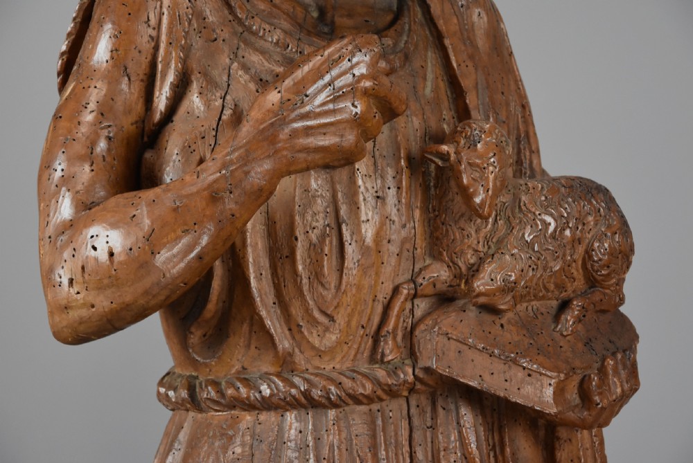 A 16th-century carved limewood figure of St. John the Baptist holding a lamb, mounted on a dark wooden base. View VIII