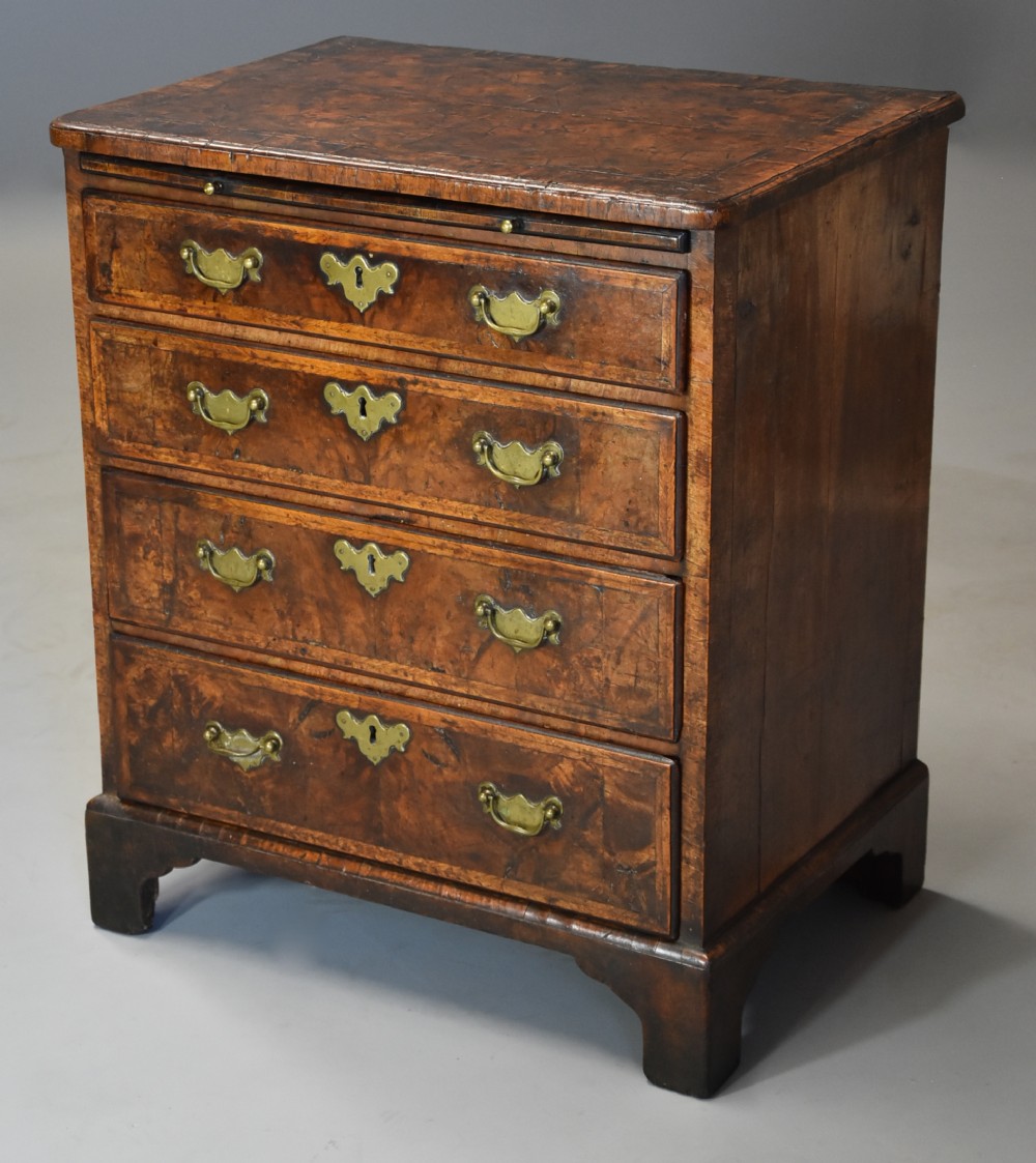 An early 18th-century walnut chest of drawers featuring four graduated drawers, brass drop handles, keyhole escutcheons, a brushing slide, and bracket feet.