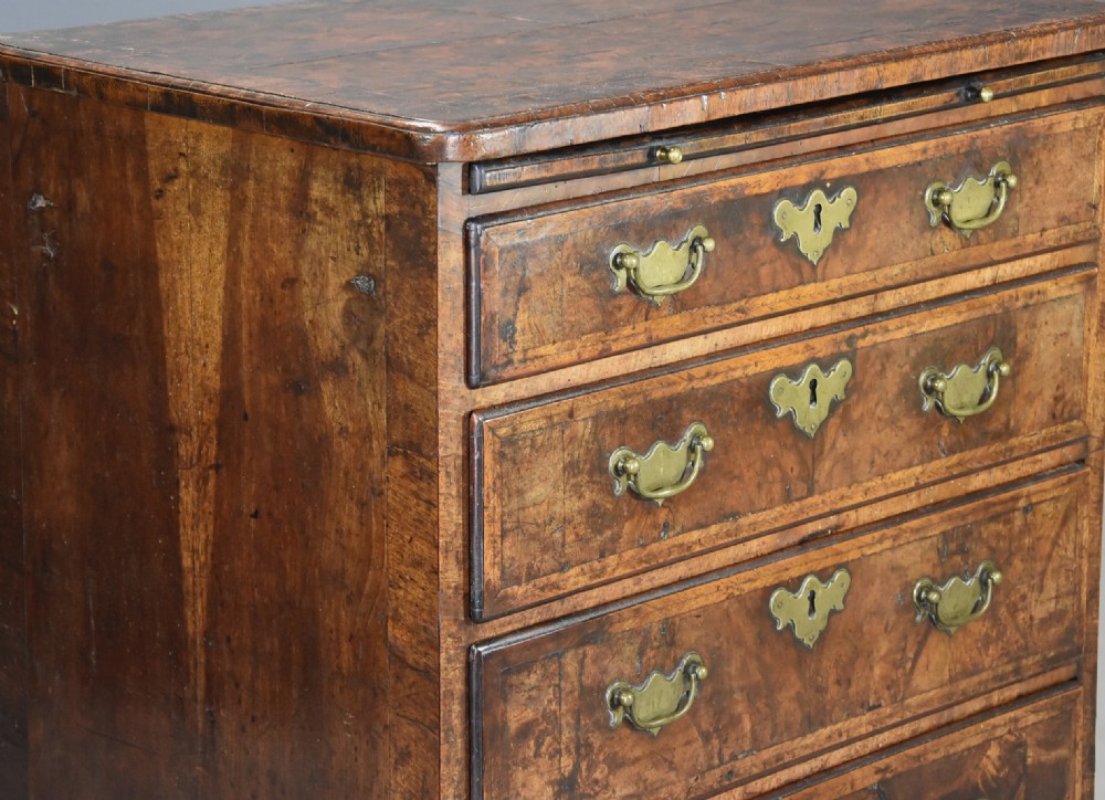 An early 18th-century walnut chest of drawers featuring four graduated drawers, brass drop handles, keyhole escutcheons, a brushing slide, and bracket feet. View IX