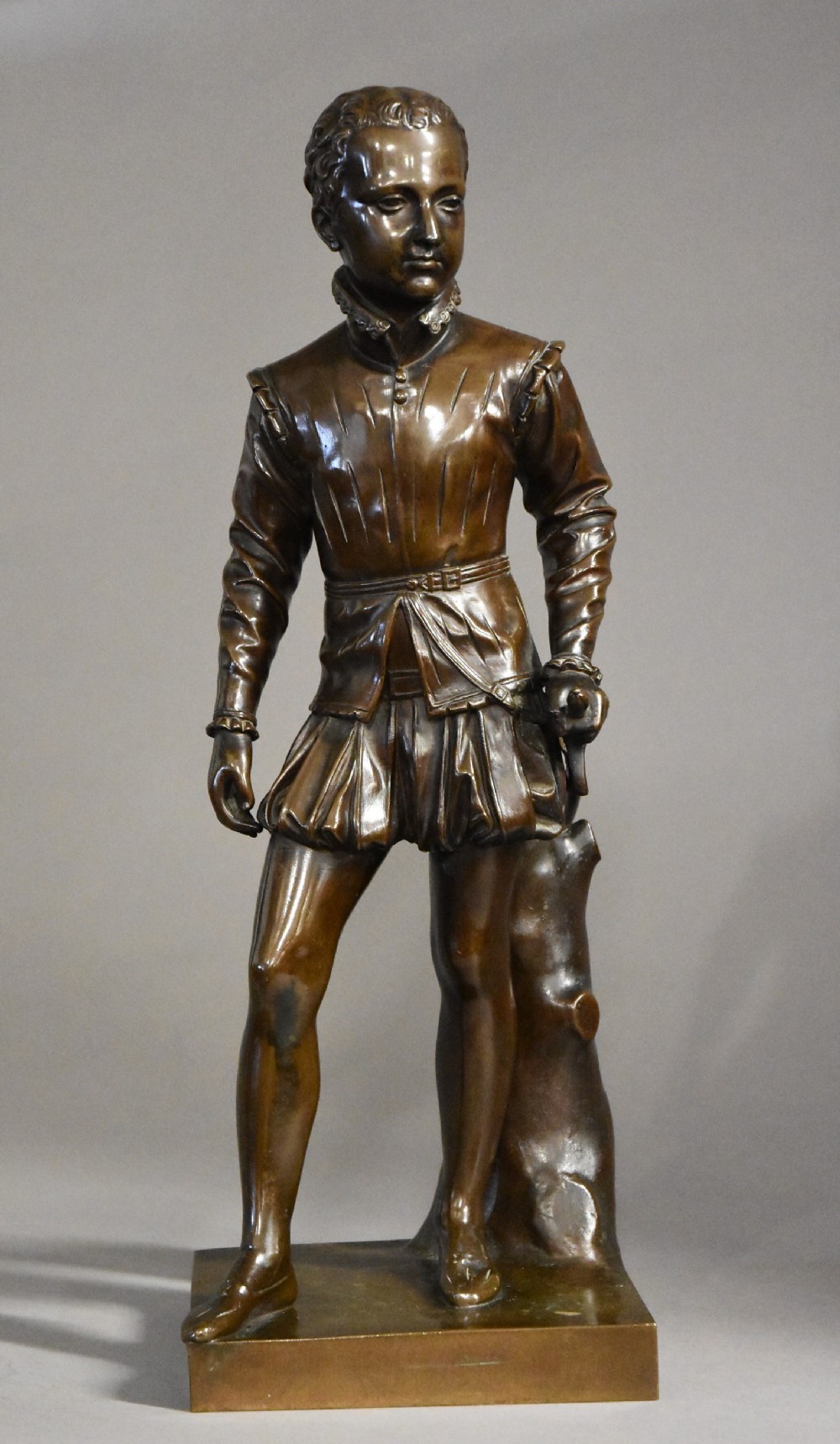 A dark brown patinated bronze standing figure of young Henry IV of France dressed in detailed Renaissance attire atop a square plinth.