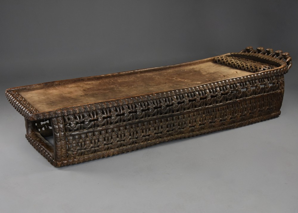 A long hand-carved dark hardwood Bamileke ceremonial bed featuring intricate openwork figurative carvings along the frame and an integrated raised headrest.