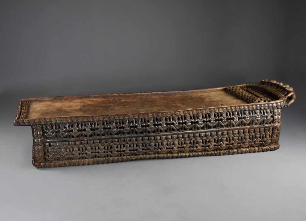 A long hand-carved dark hardwood Bamileke ceremonial bed featuring intricate openwork figurative carvings along the frame and an integrated raised headrest. View II