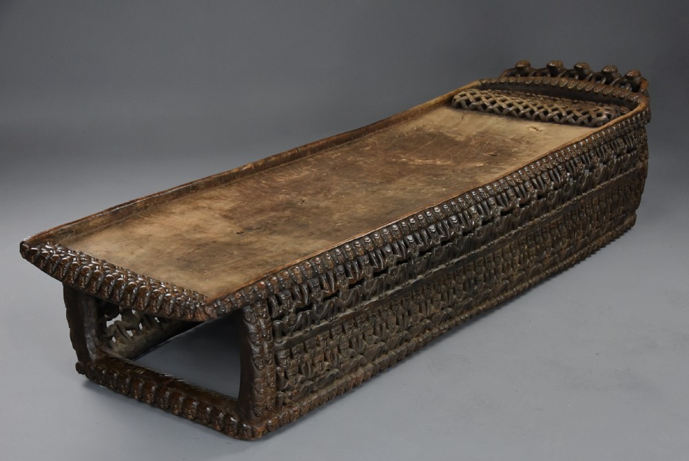 A long hand-carved dark hardwood Bamileke ceremonial bed featuring intricate openwork figurative carvings along the frame and an integrated raised headrest. View III