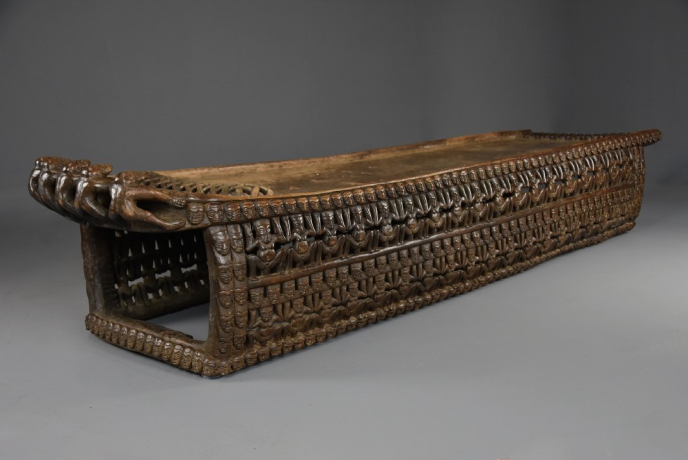 A long hand-carved dark hardwood Bamileke ceremonial bed featuring intricate openwork figurative carvings along the frame and an integrated raised headrest. View V