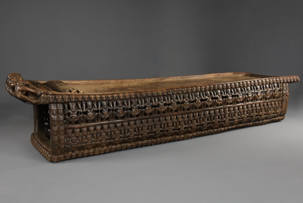 A long hand-carved dark hardwood Bamileke ceremonial bed featuring intricate openwork figurative carvings along the frame and an integrated raised headrest. View VI