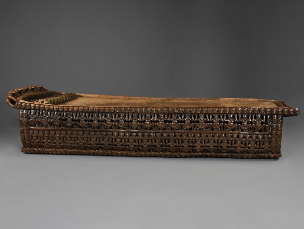 A long hand-carved dark hardwood Bamileke ceremonial bed featuring intricate openwork figurative carvings along the frame and an integrated raised headrest. View VII