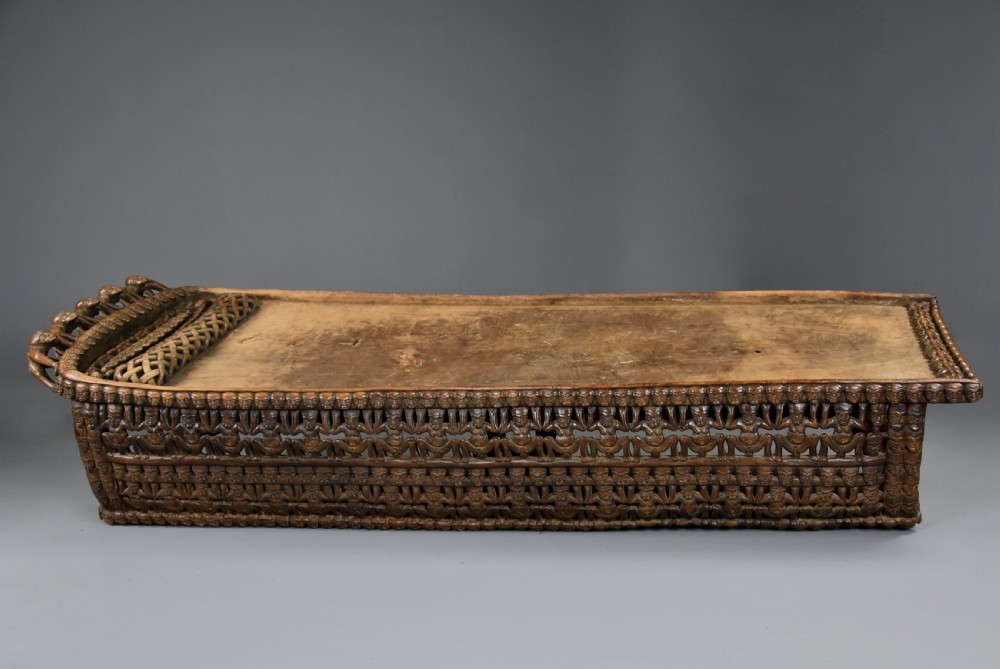 A long hand-carved dark hardwood Bamileke ceremonial bed featuring intricate openwork figurative carvings along the frame and an integrated raised headrest. View VIII