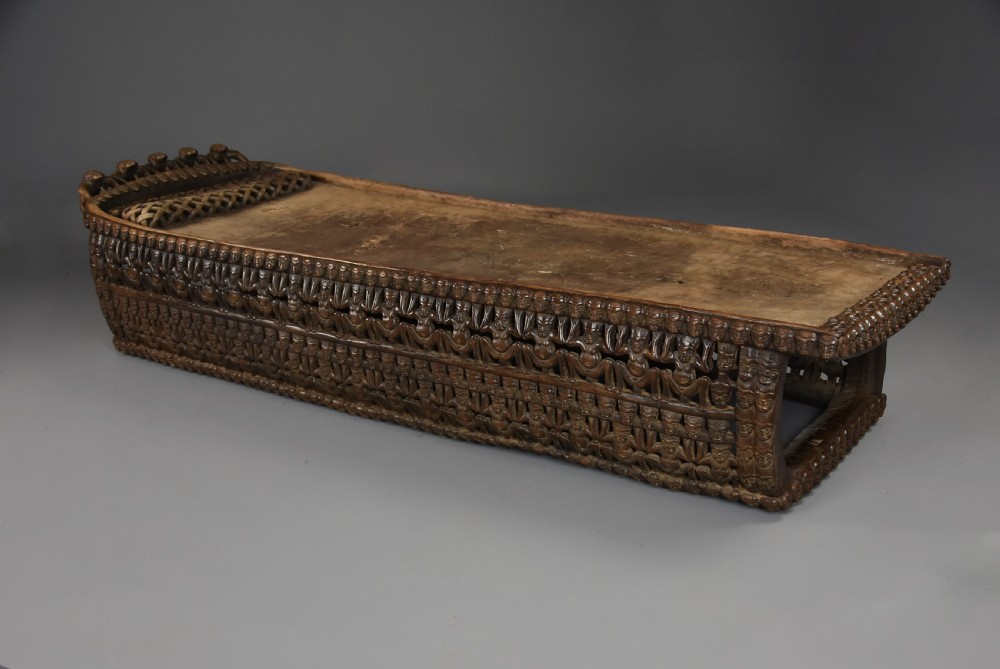 A long hand-carved dark hardwood Bamileke ceremonial bed featuring intricate openwork figurative carvings along the frame and an integrated raised headrest. View IX