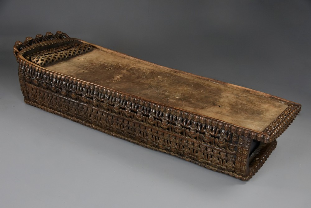 A long hand-carved dark hardwood Bamileke ceremonial bed featuring intricate openwork figurative carvings along the frame and an integrated raised headrest. View X
