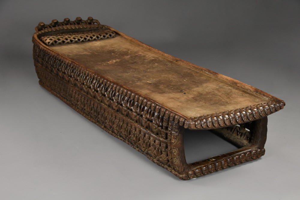 A long hand-carved dark hardwood Bamileke ceremonial bed featuring intricate openwork figurative carvings along the frame and an integrated raised headrest. View XI