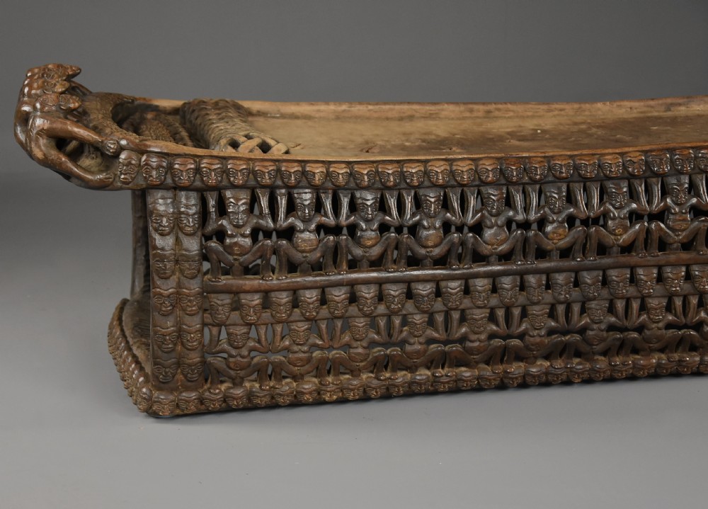 A long hand-carved dark hardwood Bamileke ceremonial bed featuring intricate openwork figurative carvings along the frame and an integrated raised headrest. View XII