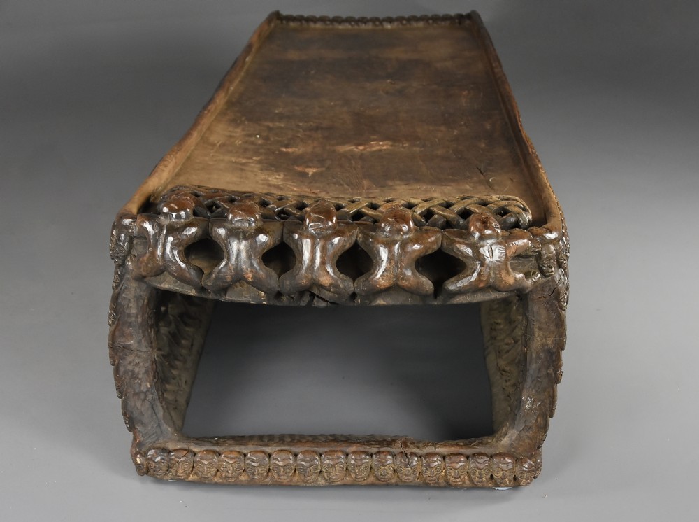 A long hand-carved dark hardwood Bamileke ceremonial bed featuring intricate openwork figurative carvings along the frame and an integrated raised headrest. View XV
