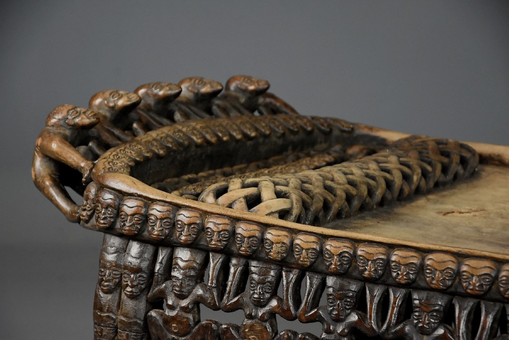 A long hand-carved dark hardwood Bamileke ceremonial bed featuring intricate openwork figurative carvings along the frame and an integrated raised headrest. View XVI