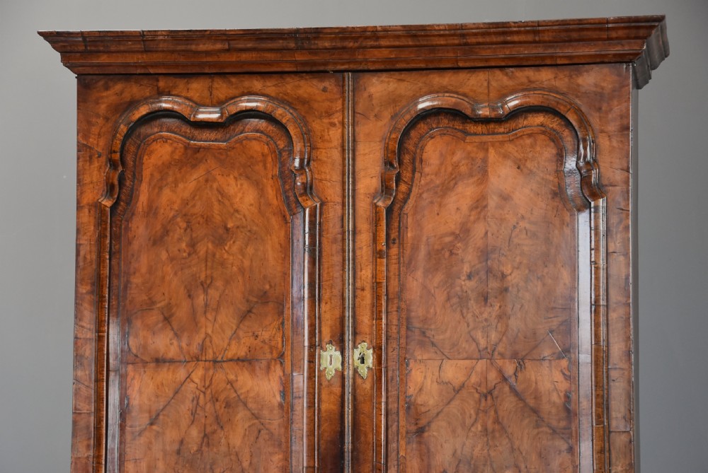 An early eighteenth-century burr walnut bureau bookcase featuring arched twin-panel upper cupboard doors, a slant-front writing slope, brass drop handles, and bracket feet. View VIII