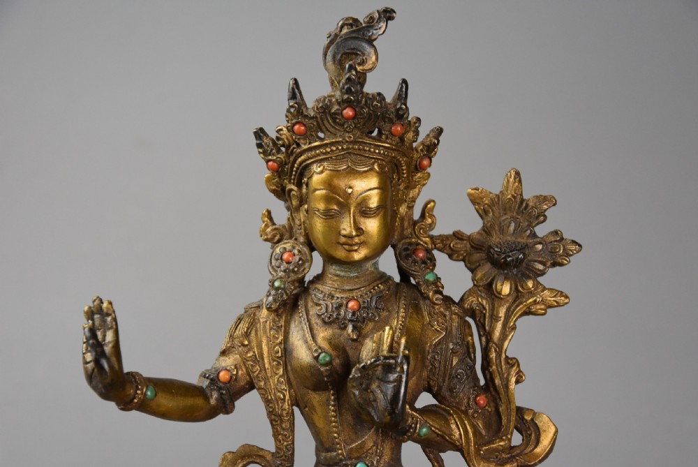 A seated gilt bronze figure of a Buddhist deity featuring an ornate crown, holding a lotus stem, with mineral inlays on a double-lotus base. View III